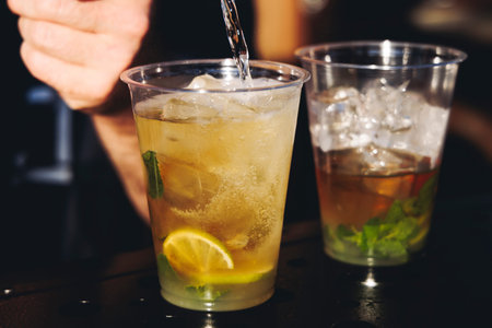 Barman mixing liquor beverages and alcohol drinks in plastic cups, bartender working, beautiful row...