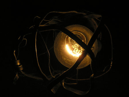 a light bulb glows in an old rusty lamp with a bent metal frame