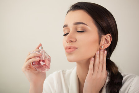 young beautiful woman holding a spray bottle of perfume and smelling aroma