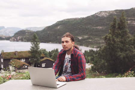 handsome freelancer guy works on a laptop in nature on the background of mountains
