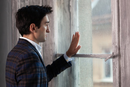a handsome man is sad near the window touching with his hand