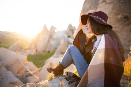 girl hiker in poncho and hat on top of mountain at sunsetの写真素材