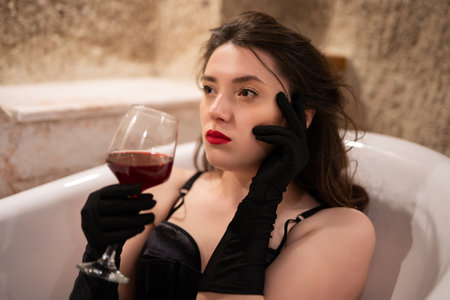 beautiful girl in erotic lingerie sitting in the bathroom with a glass of wineの写真素材