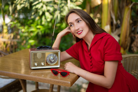 a beautiful girl in a red retro style dress listens to an antique radioの写真素材