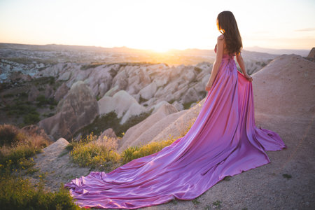 a beautiful girl in a long pink dress poses at sunset in the mountains of Cappadociaの写真素材