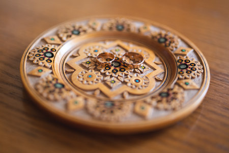 wedding rings on a traditional wooden plate with a patternの写真素材