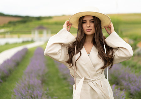 a beautiful girl with long hair and wearing a hat poses outdoors in a field of lavenderの写真素材