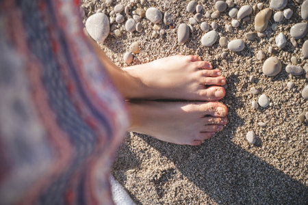 close-up photo of a girl's legs in a skirt in pebbles and sand on the beachの写真素材