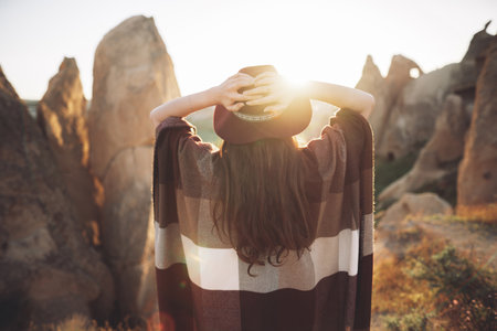 girl hiker in poncho and hat on top of mountain at sunsetの写真素材