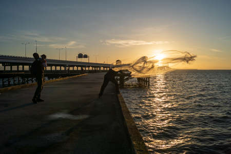 Batu Maung, Penang/Malaysia - Jan 01 2020: A man casting net to sea. Another man hug a child.のeditorial素材