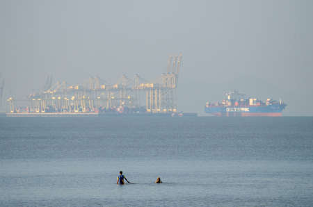 Butterworth, Penang/Malaysia - Mar 14 2020: Two man fishing at sea. Background is container terminal...