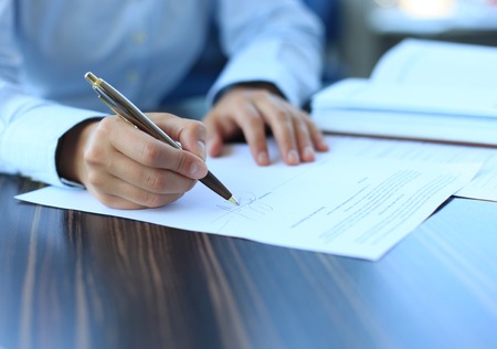 Businesswoman sitting at office desk signing a contract with shallow focus on signature