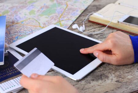 Cropped image of woman using credit card and touchpad for online tour booking on wooden table