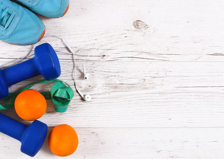 Sport equipment. Sneakers, dumbbells, measuring tape and earphones on wooden backgroundの写真素材