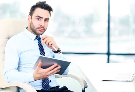 Serious young businessman working on tablet in office