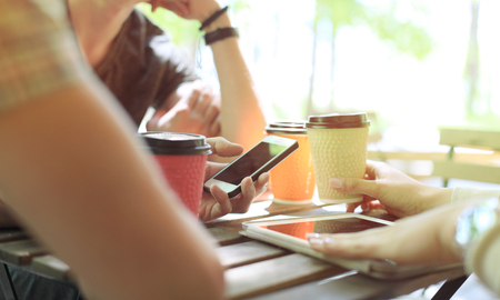 Three cheerful young people meeting and using smartphone with laptop at outdoor cafe.の写真素材