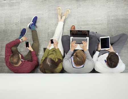 Group of attractive young people sitting on the floor using a laptop, Tablet PC, smart phones,...