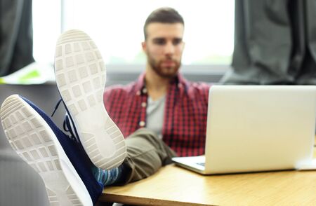 Portrait of a very relaxed young designer leaning back on his desk and putting his feet up his desk at the office.の写真素材