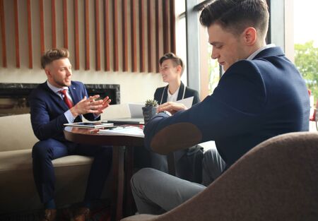 Businessman looks at his wrist watch checking the time. Businessperson sitting a meeting and working at background.の写真素材