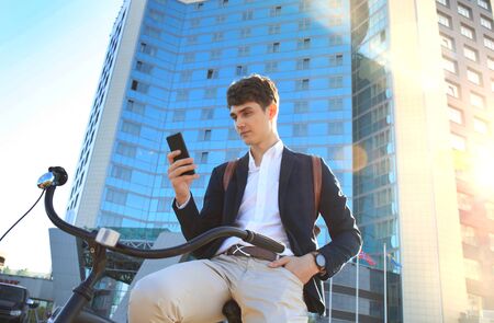 Young businessman with bicycle and smartphone on city streetの写真素材