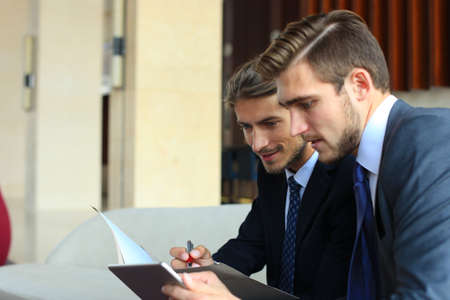 Two young businessmen using touchpad at meetingの写真素材