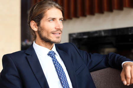 Portrait of happy young businessman sitting on sofa in hotel lobbyの写真素材