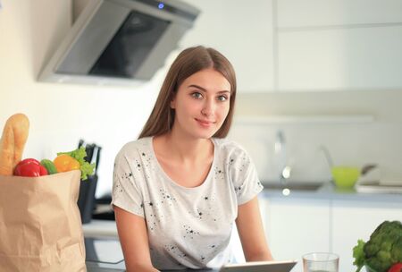 Young woman holding grocery shopping bag with vegetables standing in the kitchen.