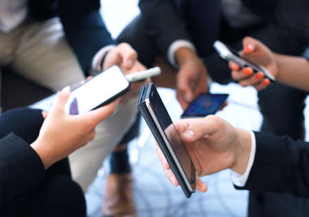 Group of people using smart phones sitting at the meeting, close up on hands.