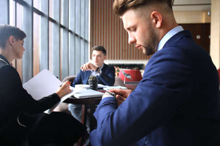 Businessman looks at his wrist watch checking the time. Businessperson sitting a meeting and working at background.の写真素材