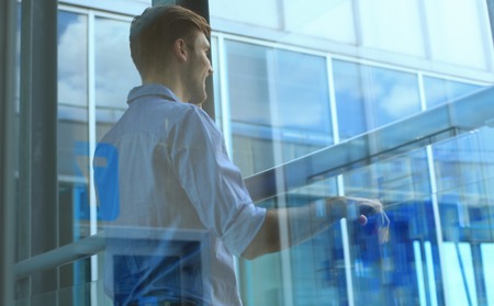 Young man standing near window in his office while thinking about his goals.
