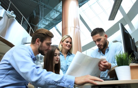 Group of young modern people in smart casual wear having a brainstorm meeting while standing in the...