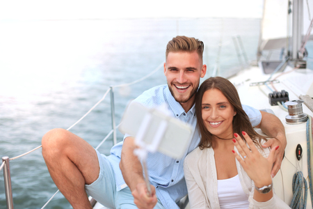 Happy couple taking a selfie after engagement proposal at sailing boat, relaxing on a yacht at the sea.の写真素材