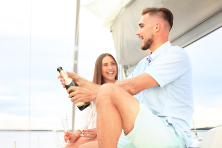 Smiling young couple with champagne and looking at each other while sitting on the board of yacht.の写真素材