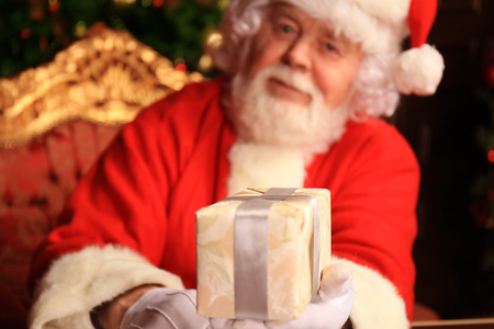 Portrait of happy Santa Claus sitting at his room at home near Christmas tree with gift box.の写真素材