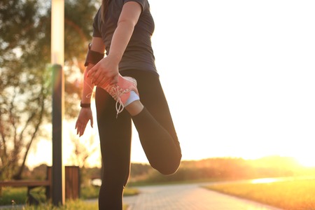 Young attractive sporty fitness woman runner warming up before run at sunset or sunrise on city.の写真素材