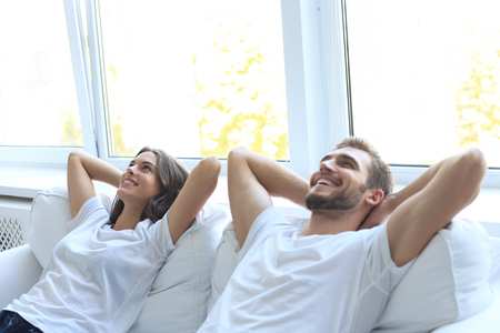 Smiling beautiful couple sitting on a sofa and dreaming about new home.の写真素材