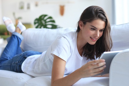 Beautiful young woman using tablet sitting on sofa at home at living room.の写真素材