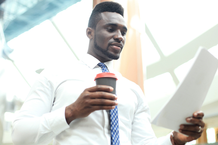 Successful African American businessman reading paper at workplace, looking at financial document, holding coffee.の写真素材