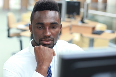 Portrait of successful African-American businessman sitting at desk with computer in office.の写真素材