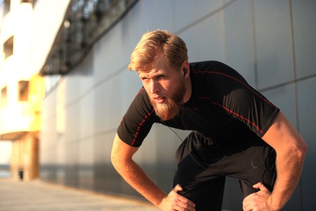 Handsome young man after run resting after jog in the city at sunset or sunrise.