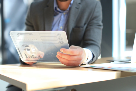 Future concept. Businessman analyzing financial statistics displayed on the futuristic transparent tablet screen.の写真素材