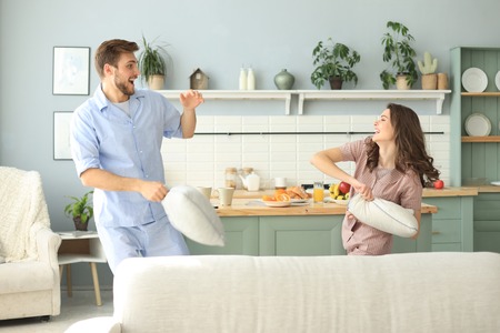 Happy loving couple having fun while having a pillow fight in the living roomの写真素材