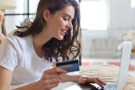 Happy natural brunette using credit card and laptop in bedroomの写真素材