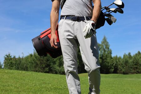 Cropped image of male golfer carrying golf bag with drivers while walking by green grassの写真素材