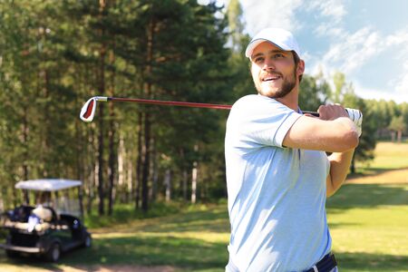 Golfer hitting golf shot with club on course while on summer vacationの写真素材