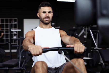 Fit and muscular man using rowing machine at gym