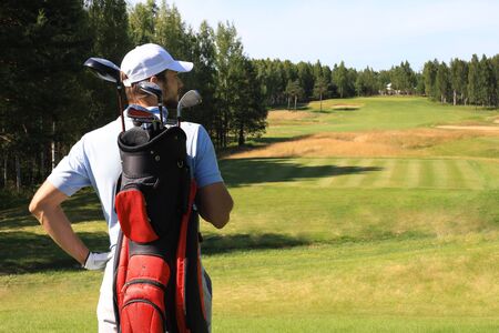 Golf player walking and carrying bag on course during summer game golfingの写真素材