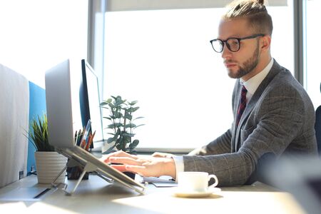 Good looking young man in full suit using laptop while sitting in the office