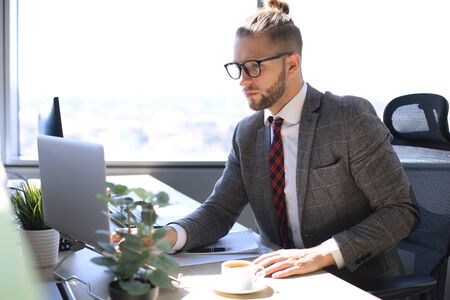 Good looking young man in full suit using laptop while sitting in the office