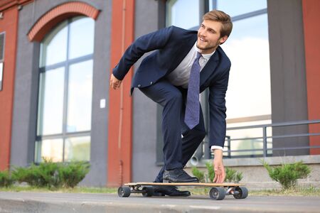 Confident young businessman in business suit on longboard hurrying to his office, on the street in the city.の写真素材